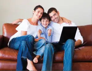 Young mother and father sitting on brown couch holding there child and laptop ready to sell there home.
