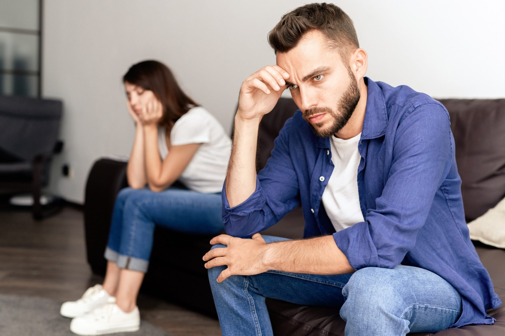 Frustrated young couple being wronged each other sitting on sofa in living room and not talking because of home purchase.